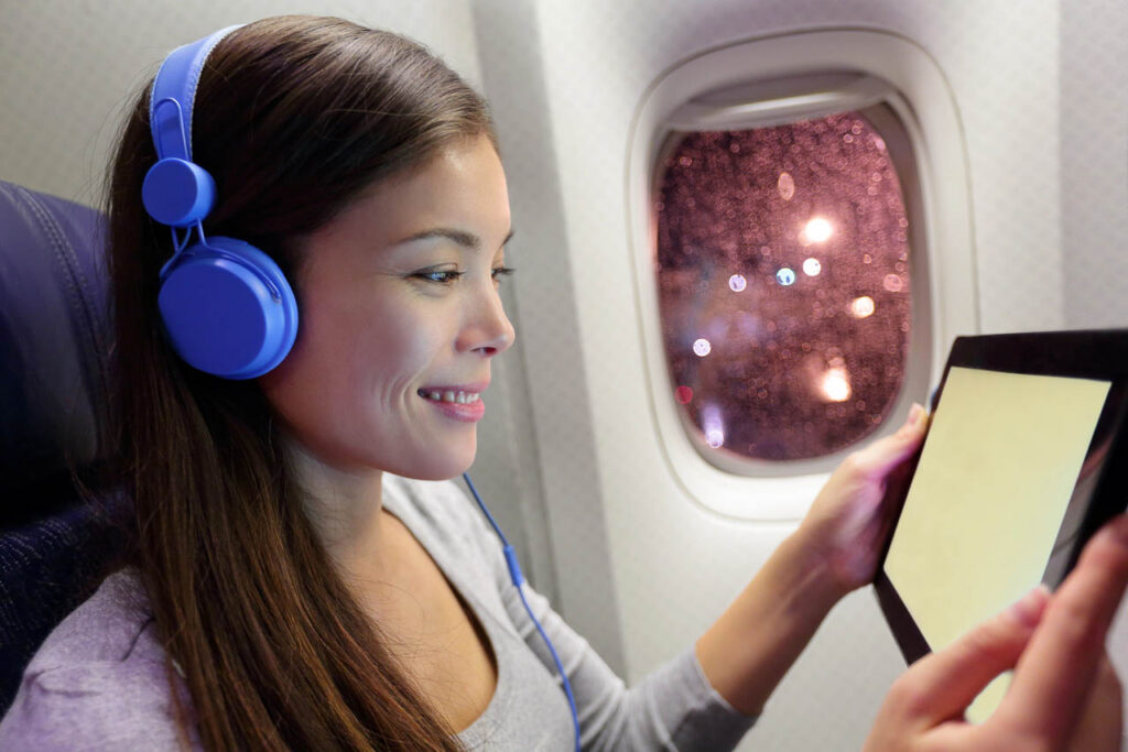 Passenger in airplane using tablet computer. Woman in plane cabin using smart device listening to music on headphones.